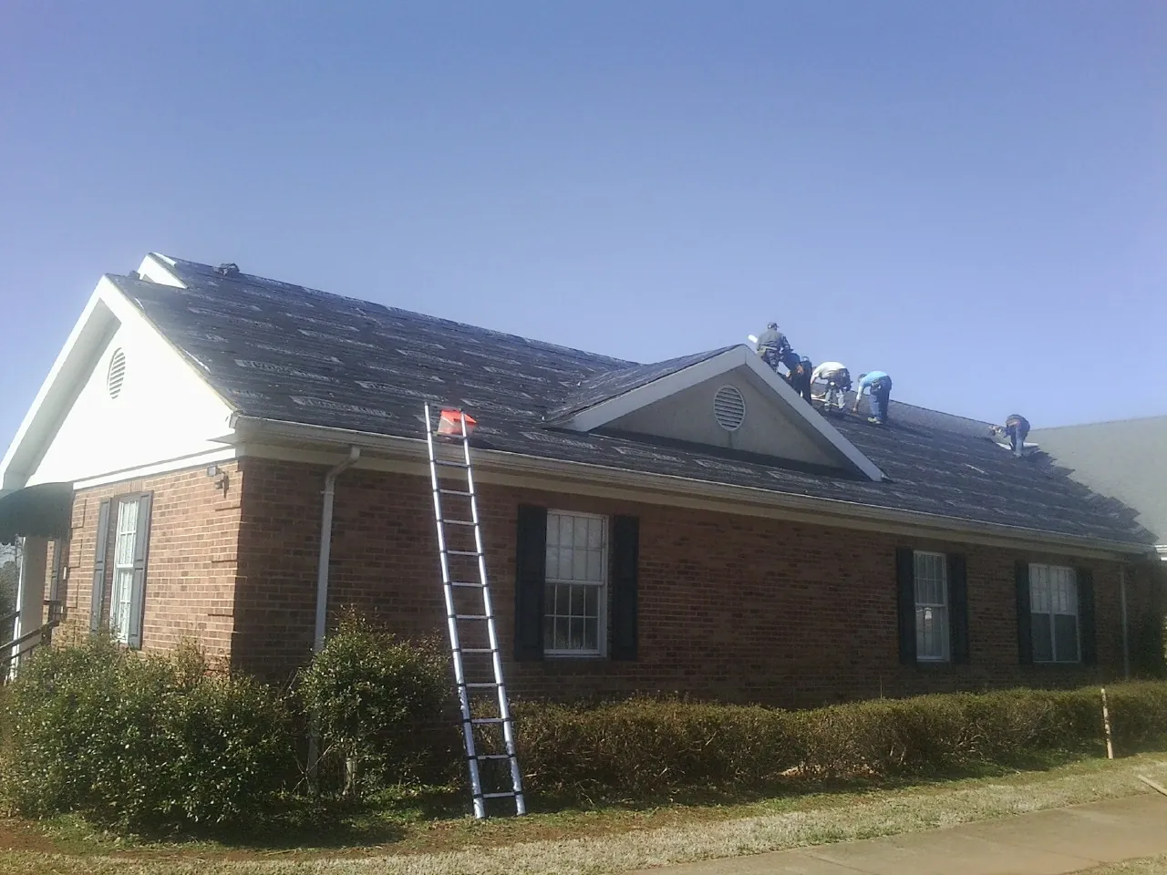 Crew tearing shingles off a brick ranch roof with a ladder set — Emergency Roof Repair work by our crew in Middleboro