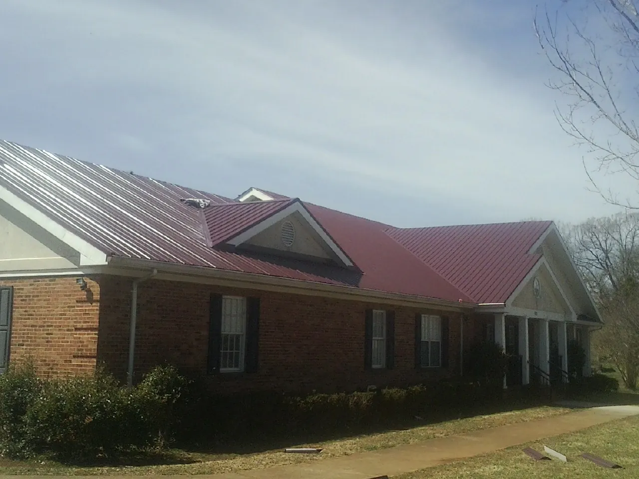 Red metal roof with gabled entries on a long brick building, from a Hail Damage Roof Repair job in Middleboro