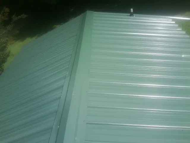 New green metal panels meeting at the ridge of a roof — Flat Roof Repair work by our crew in Middleboro