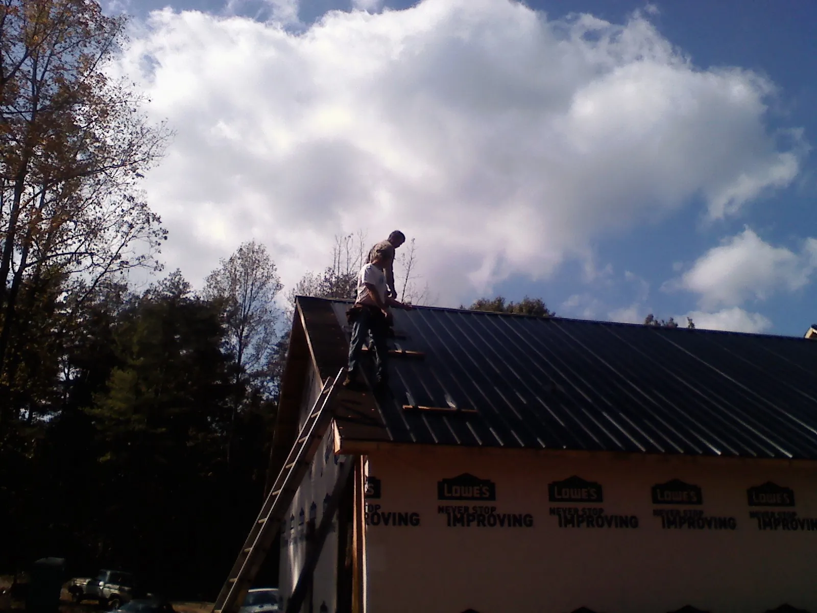 Roofer fastening dark metal panels high against a cloudy sky, from a Roof Inspection job in Middleboro