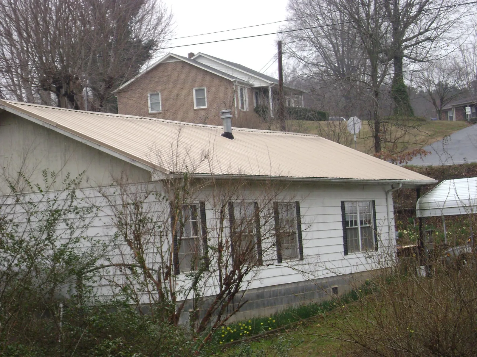 Tan metal roof on a white sided house set into a hillside — Commercial Roofing by Roofing Brothers in Middleboro
